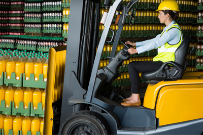 Operaria de carretillas moviendo mercancía en almacén de bebidas.